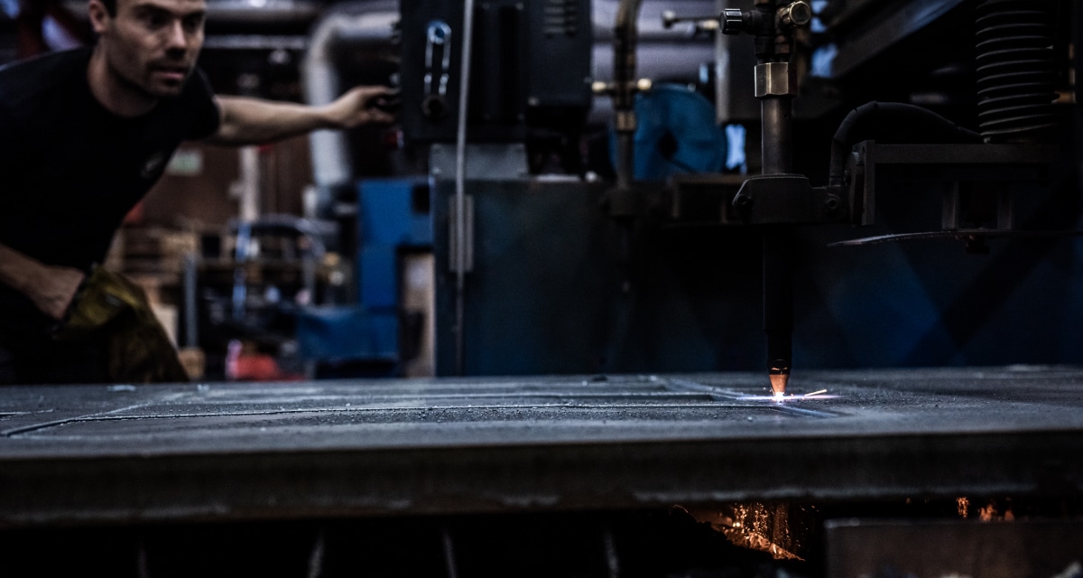 En person driver en maskin som skär en metallplåt med en stark låga i en industriell miljö.