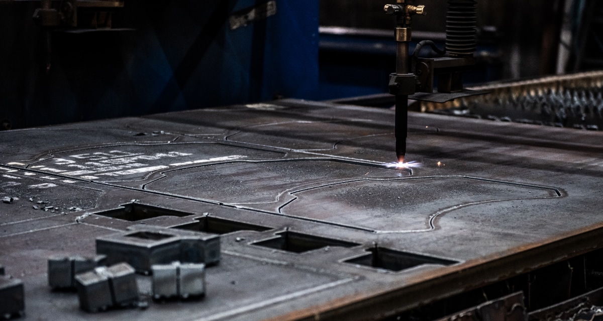 En metallbearbetningsmaskin skär intrikata mönster till en metallplåt, omgiven av utskurna bitar.