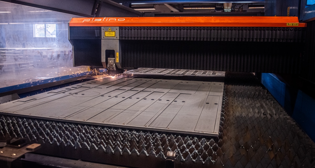 En stor industrimaskin skär en metallplåt, med synliga gnistor nära skärområdet.