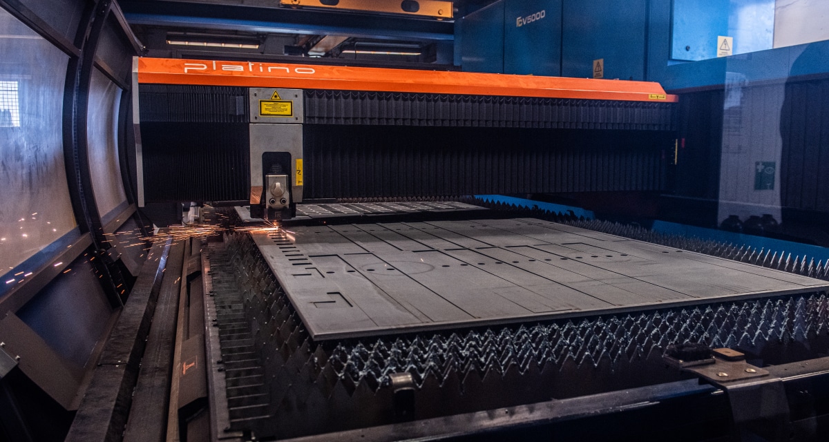 En CNC-laserskärmaskin som arbetar på en metallplåt med gnistor synliga vid skärpunkten.